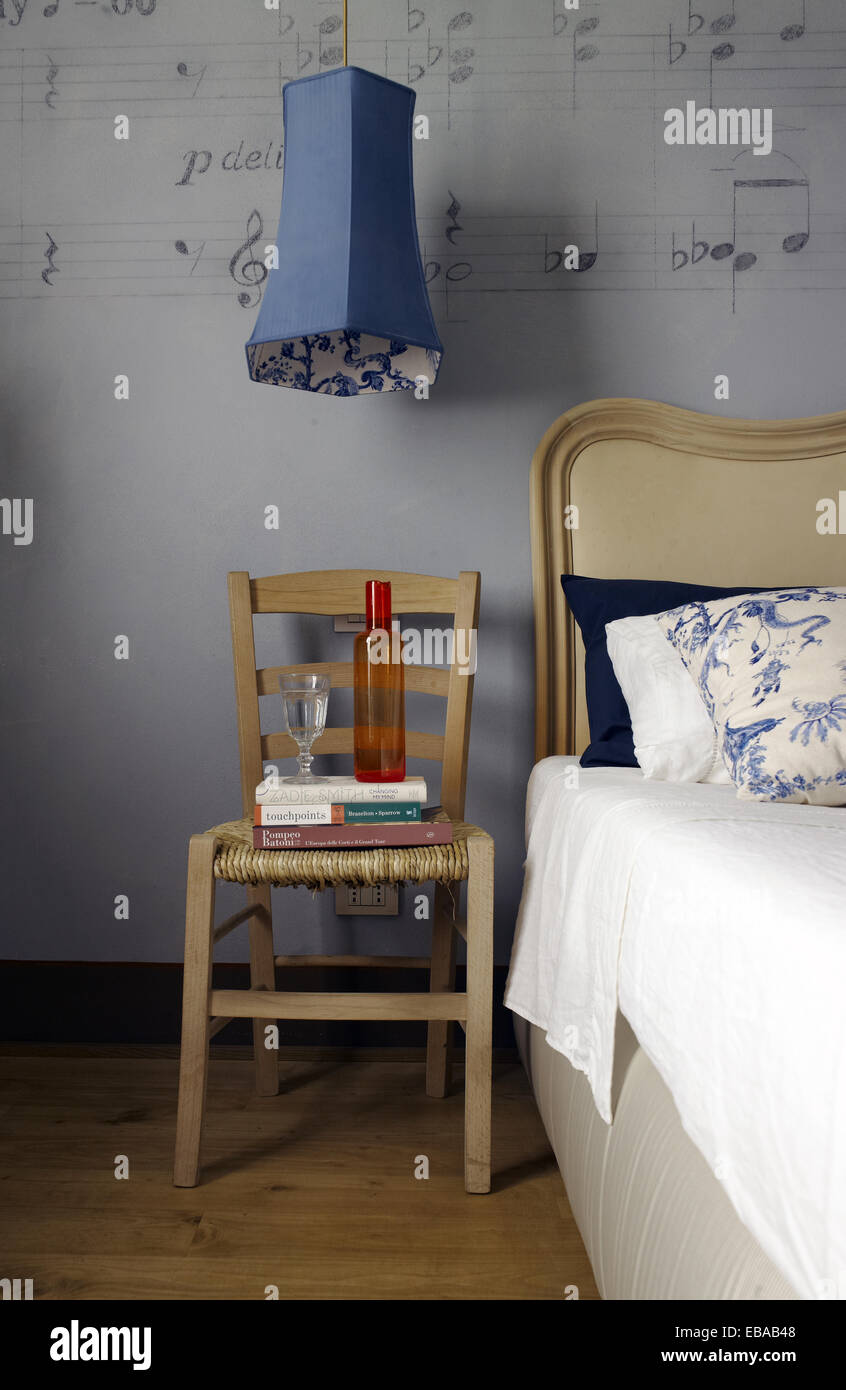 Accueil décoration : Détail d'une chambre à coucher avec une chaise et mur décoré. Une chaise avec une bouteille d'eau et un verre Banque D'Images