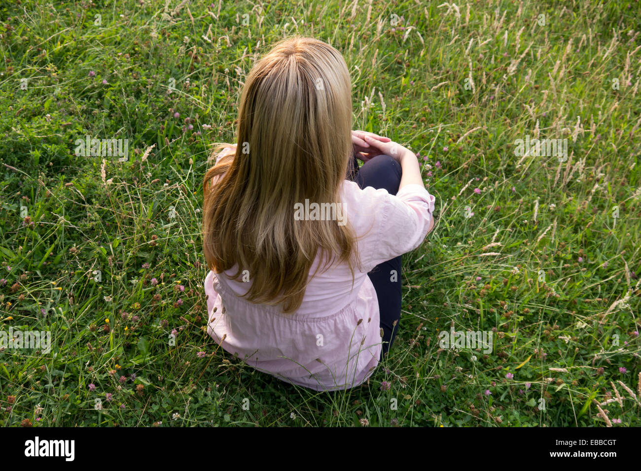 De longs cheveux blond woman sitting on meadow Banque D'Images