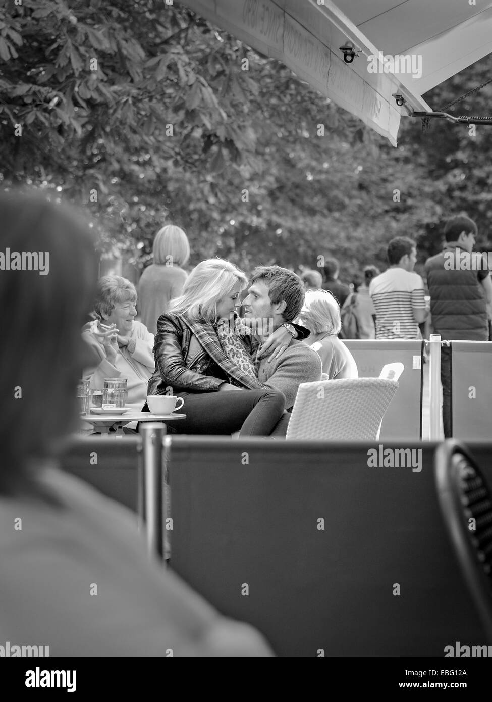 Couple embrassant. Image candiée d'un jeune couple insouciant et affectueux dans un café pavé. Photographie britannique noir et blanc Banque D'Images