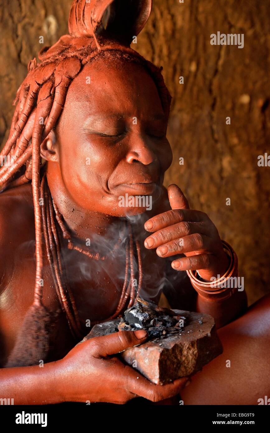 Femme Himba habillé de façon traditionnelle dans sa hutte, l'application de parfum, Purros Village traditionnel, Purros, Kaokoland, Kunene, Namibie Banque D'Images