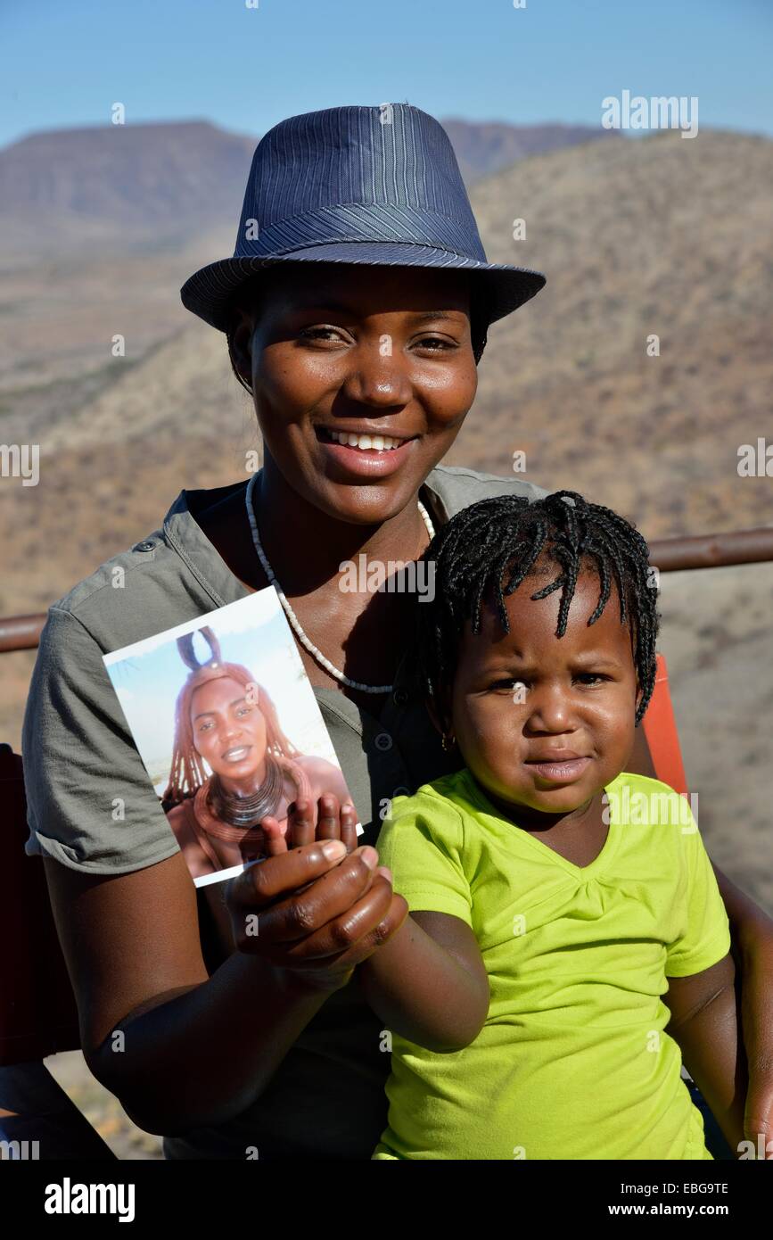 Femme Himba moderne tenant son enfant avec une photo d'elle portant des vêtements traditionnels, Orupembe, Kaokoland, Kunene, Namibie Banque D'Images