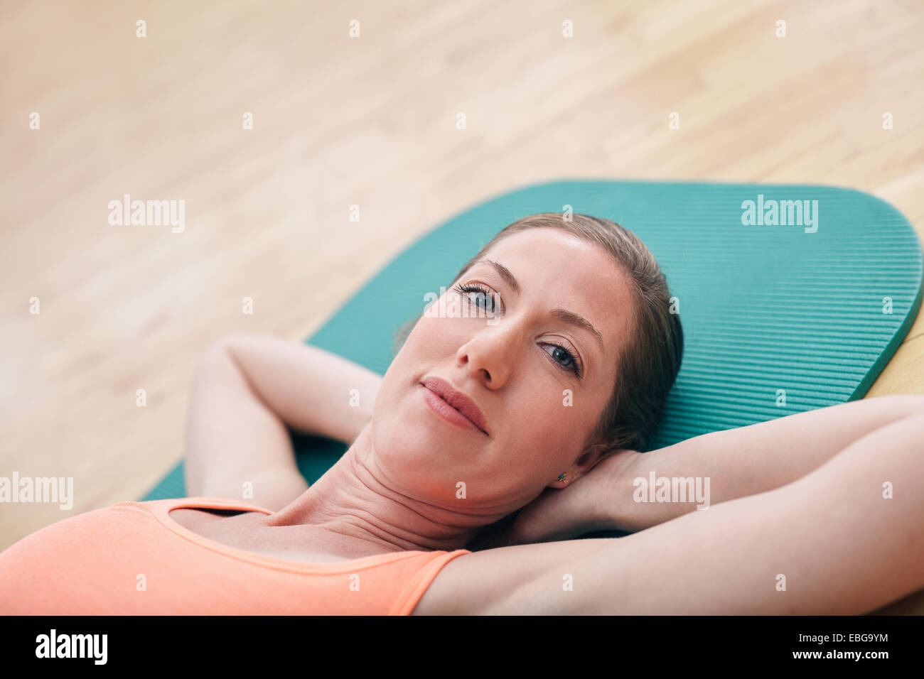 Photo de belle femme couchée sur le plancher du gymnase avec les mains derrière la tête. Fit woman lying on exercise mat looking at camera. Banque D'Images