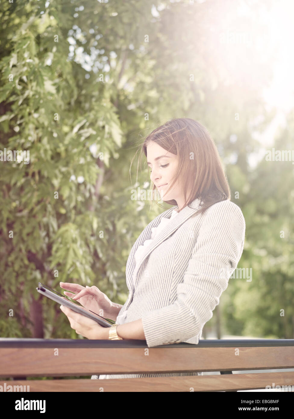 Femme portant un costume d'affaires avec un ordinateur tablette debout derrière un banc de parc, Innsbruck, Tyrol, Autriche Banque D'Images