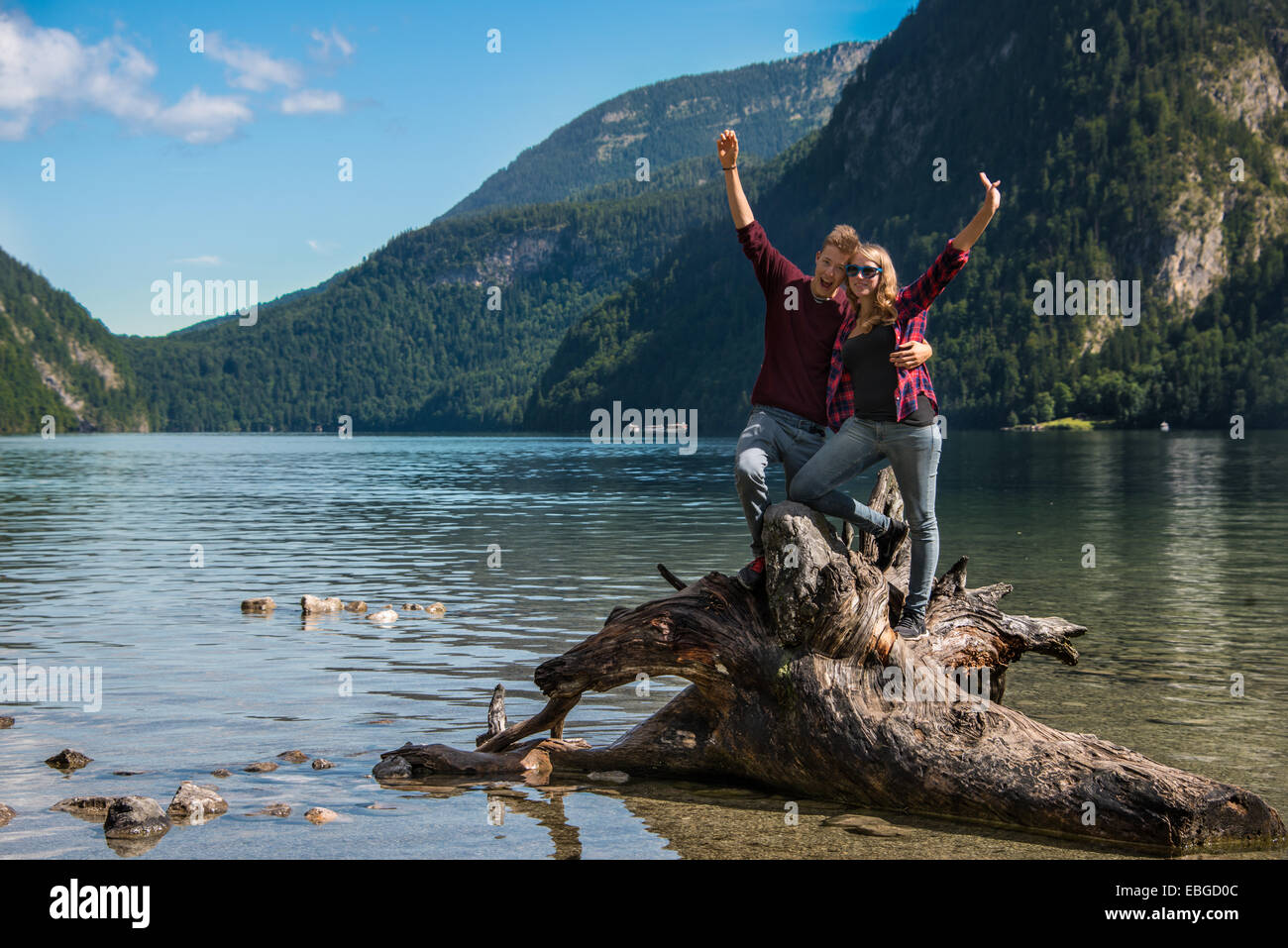 Jeune couple sur un tronc d'arbre tombé s'étendant leurs bras en l'air, parc national de Berchtesgaden, Königssee Banque D'Images