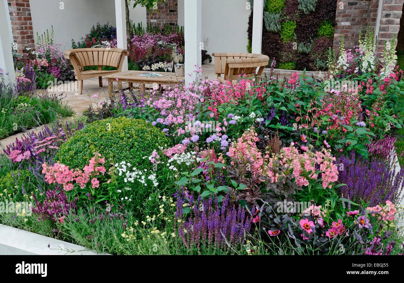 Un jardin contemporain avec terrasse et un élégant mobilier en bois entouré de fleurs colorées frontières Banque D'Images