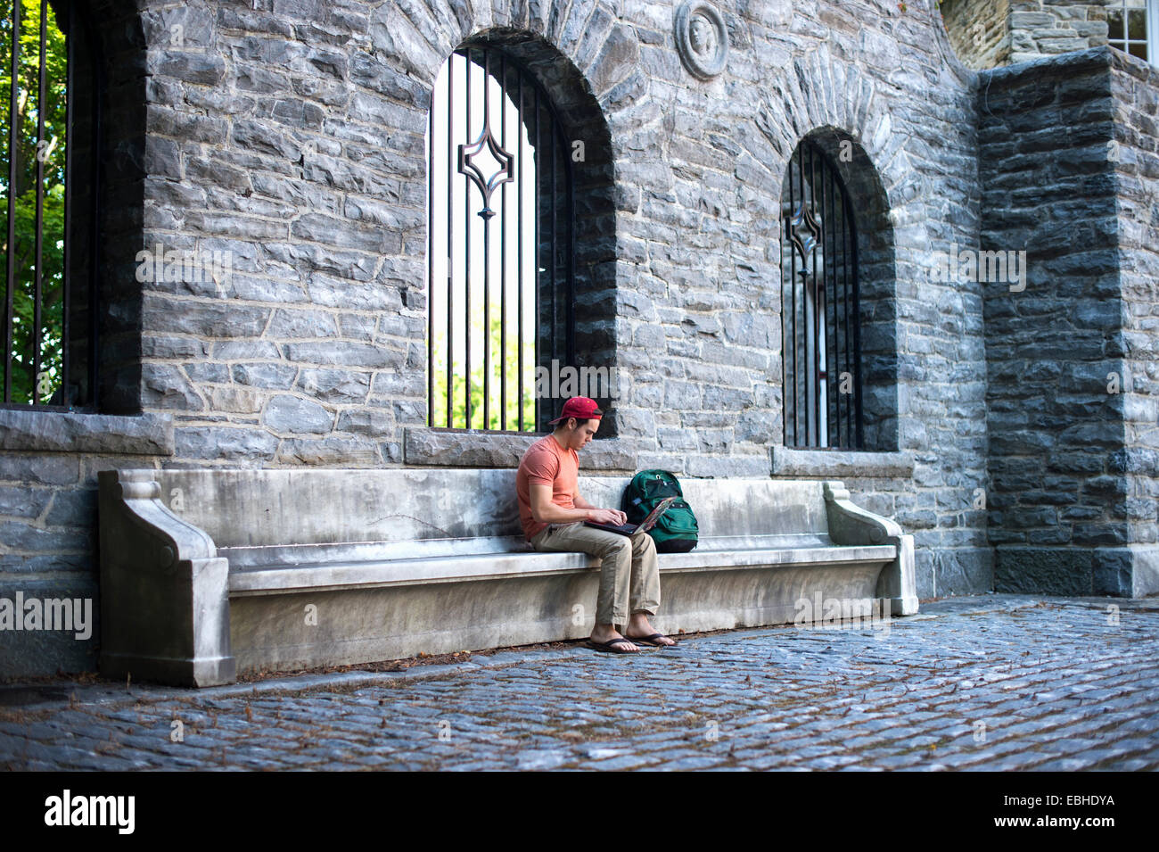 Male student sitting on bench using laptop Banque D'Images
