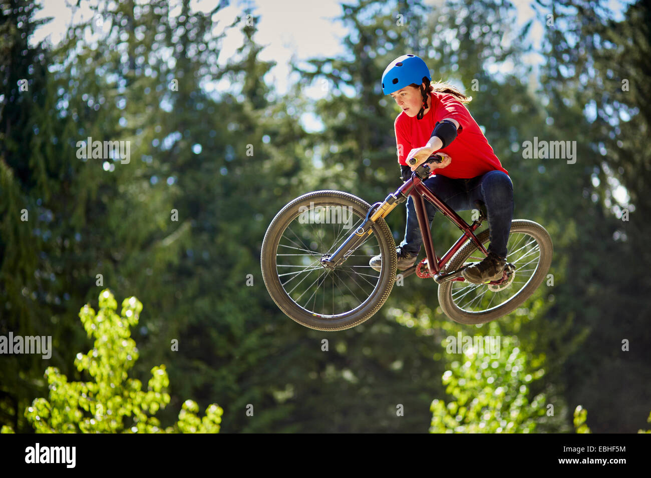 Jeune femme biker bmx jumping mid air en forêt Banque D'Images