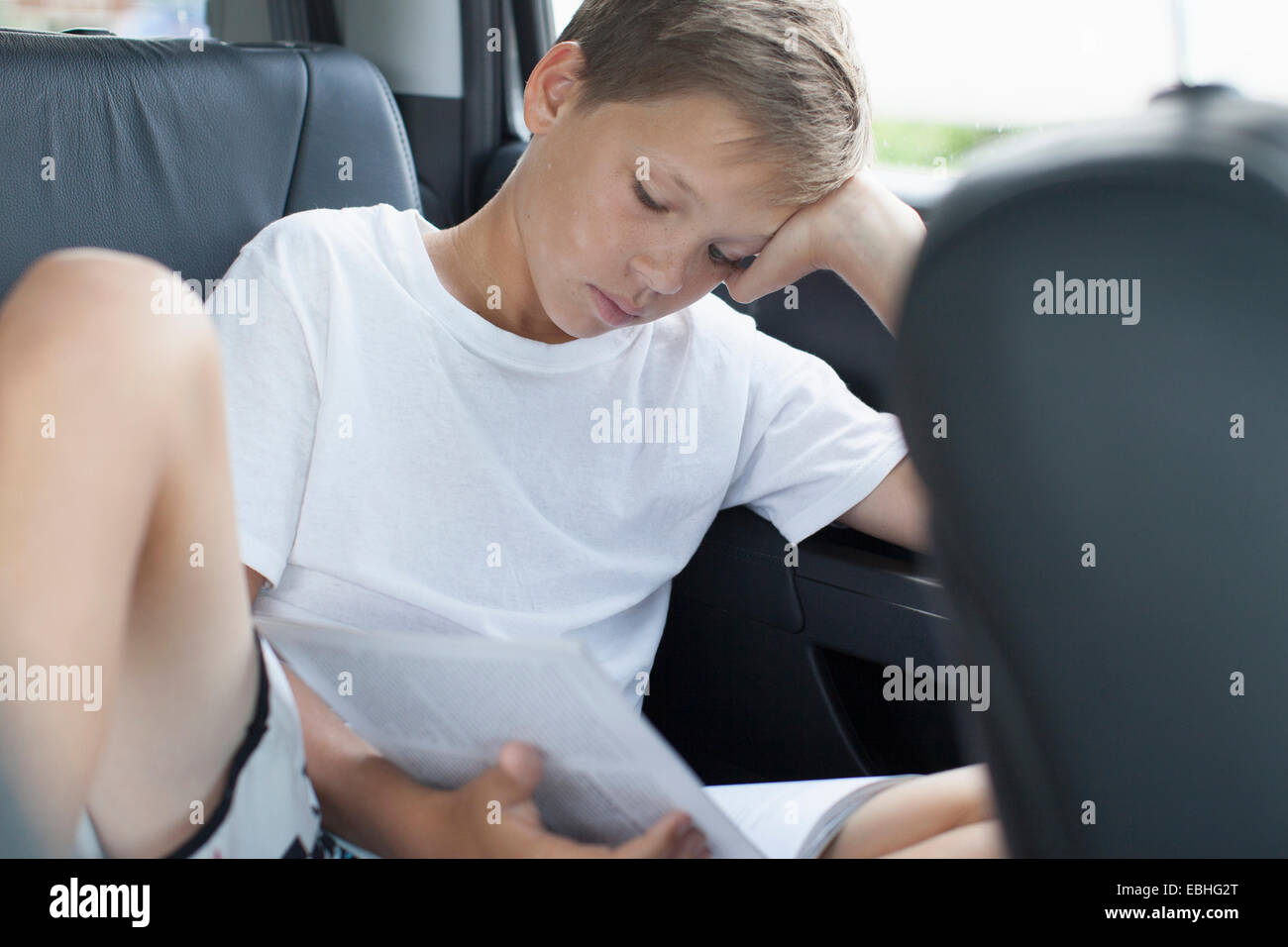 Teenage boy reading in back seat of car Banque D'Images