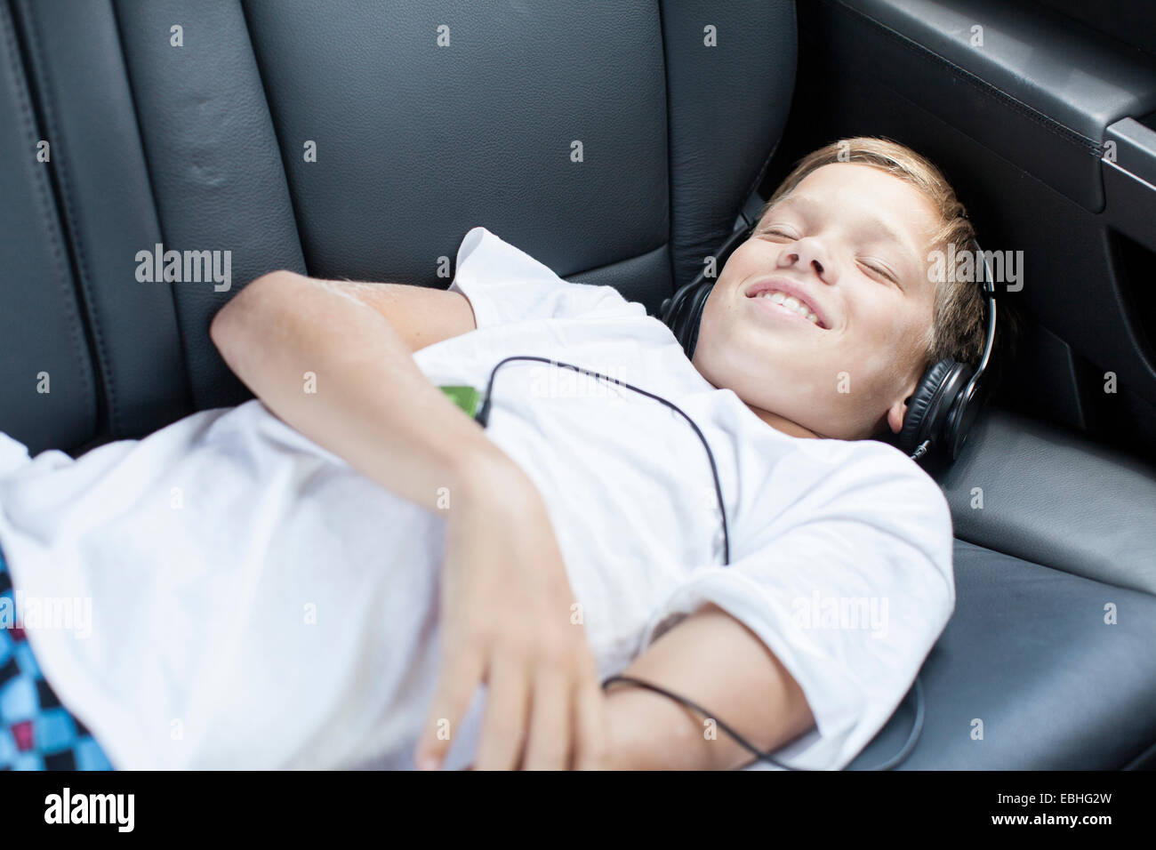 Teenage boy smiling pendant l'écoute au casque in back seat of car Banque D'Images