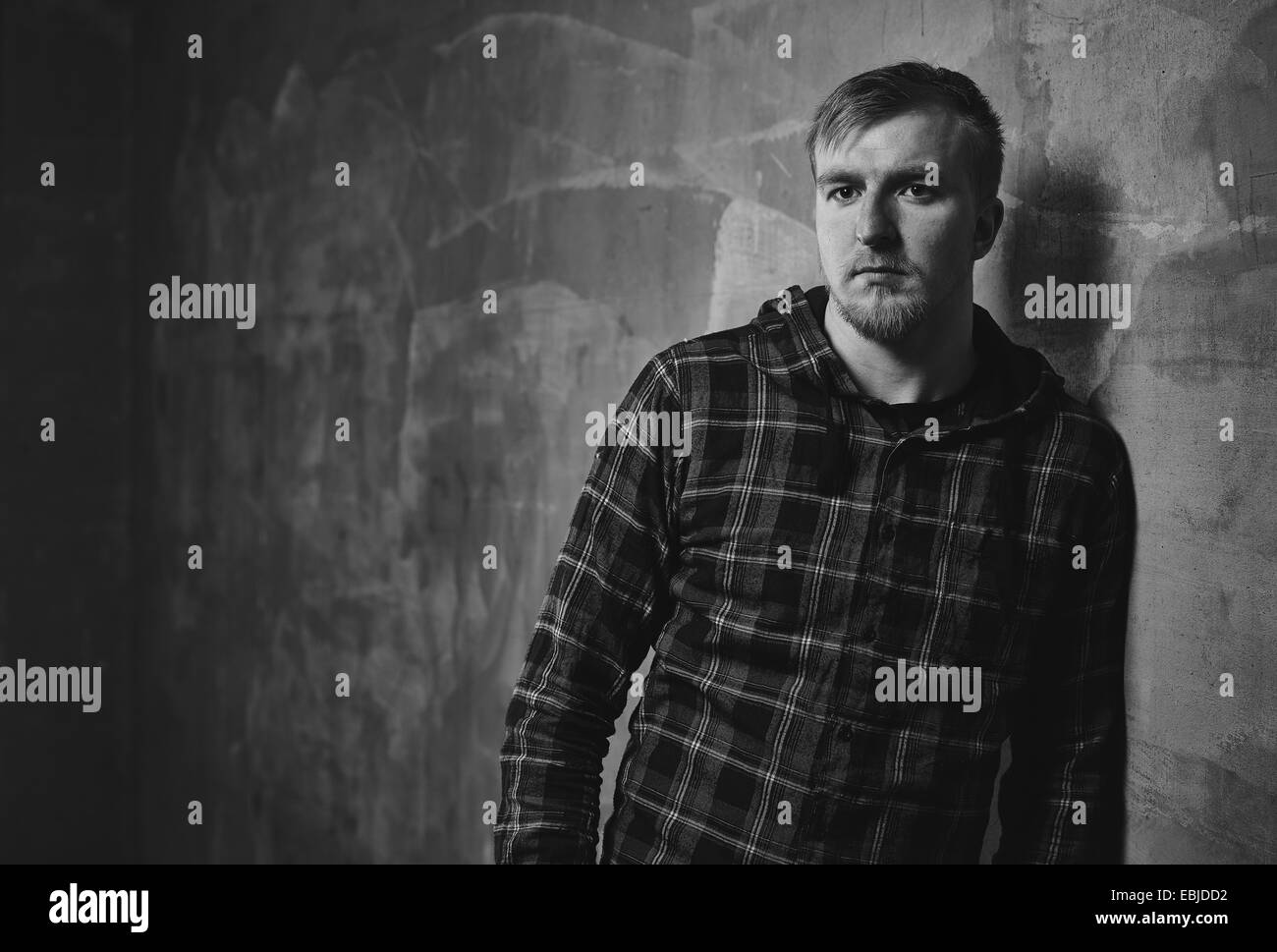 Beau jeune homme portant une chemise à carreaux et qu'il s'appuyer contre le mur en béton - l'image en noir et blanc Banque D'Images