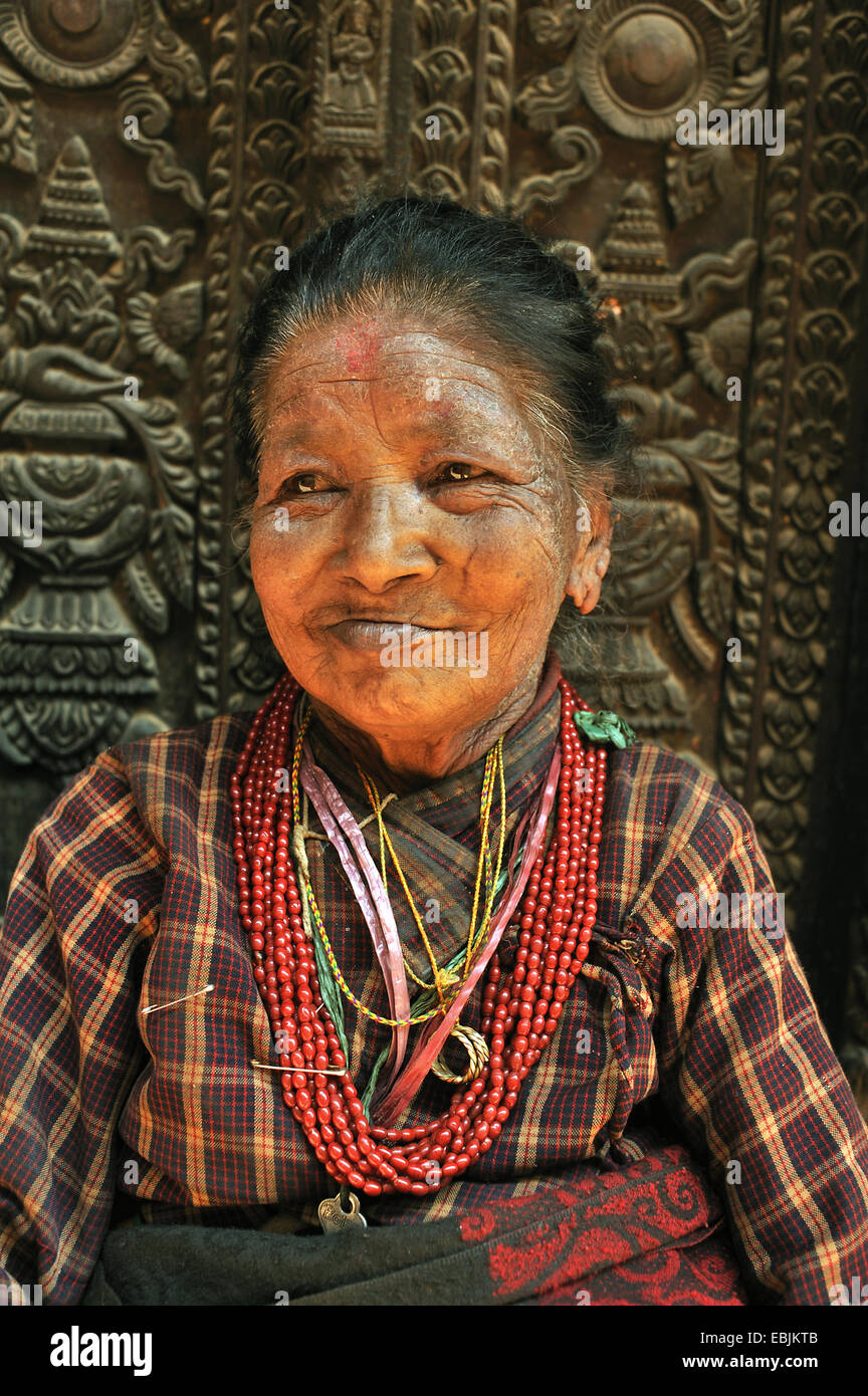 Portrait d'une vieille femme en face d'une porte en bois du palais du roi orné de sculptures, Népal, Patan Banque D'Images