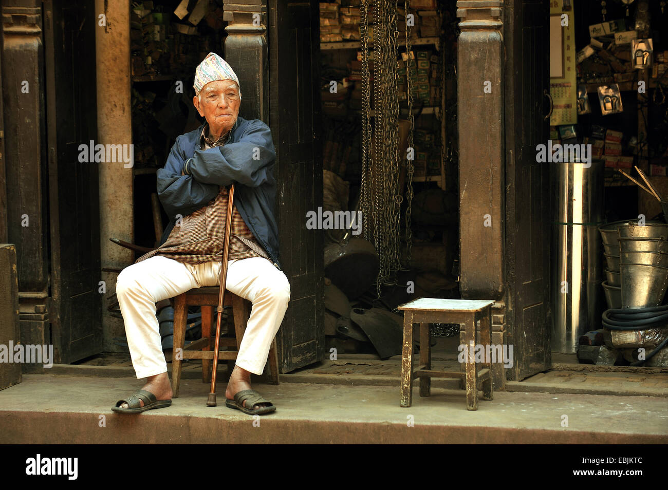 Vieil homme coin sur une chaise en face d'une boutique, Népal, Patan Banque D'Images