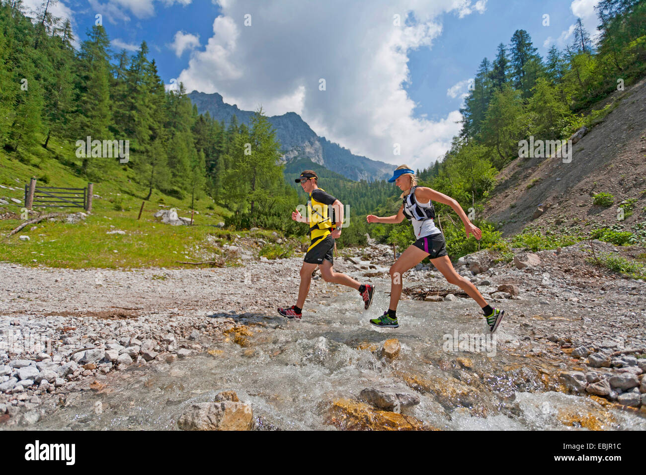 Jeune couple traversant un ruisseau en sautant tout en course en sentier dans la montagne Dachstein, Autriche, Styrie, Dachstein Banque D'Images