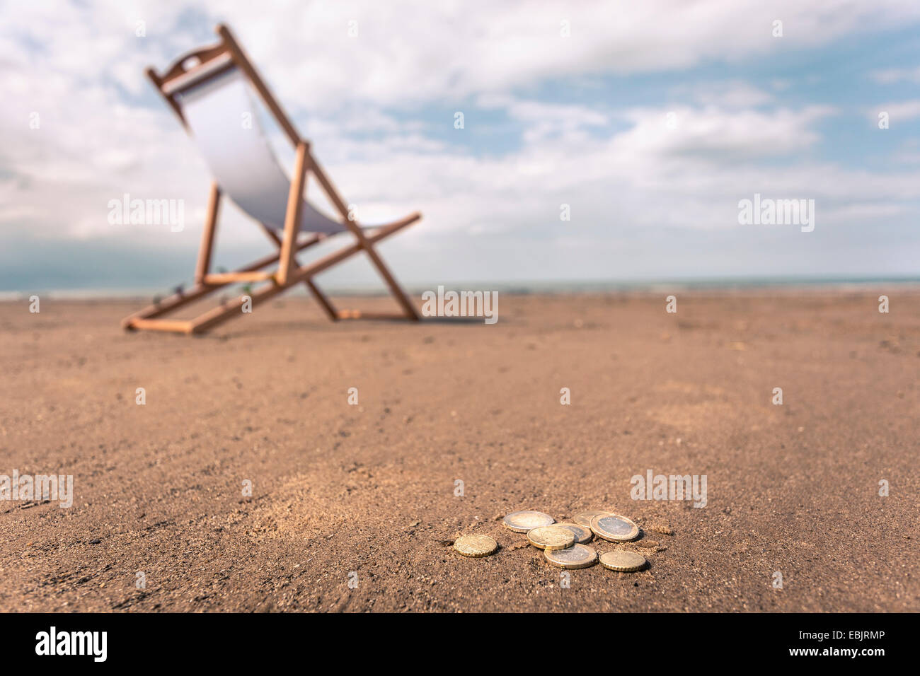 Chaise longue sur la plage, des pièces de monnaie sur le sable en premier plan Banque D'Images