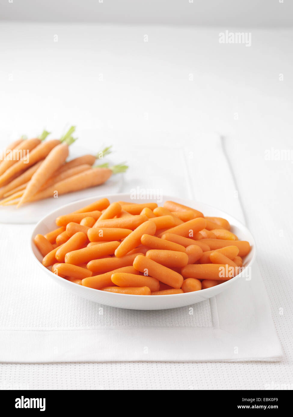 Des carottes crues sur une planche à découper en marbre et bol de carottes bouillies Banque D'Images