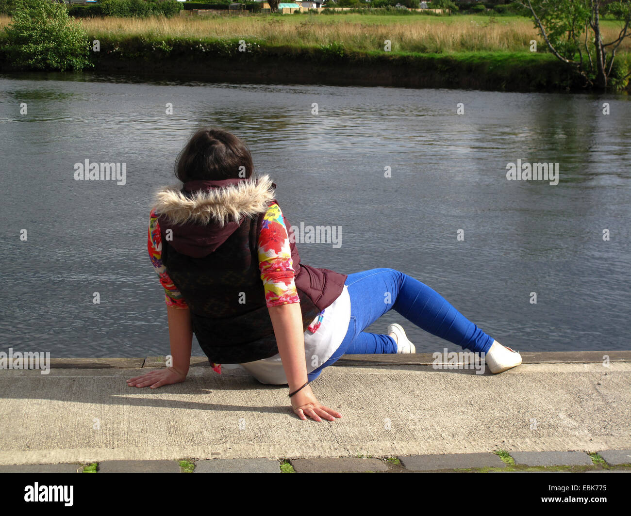 Jeune fille assise à côté de la rivière vue arrière Banque D'Images