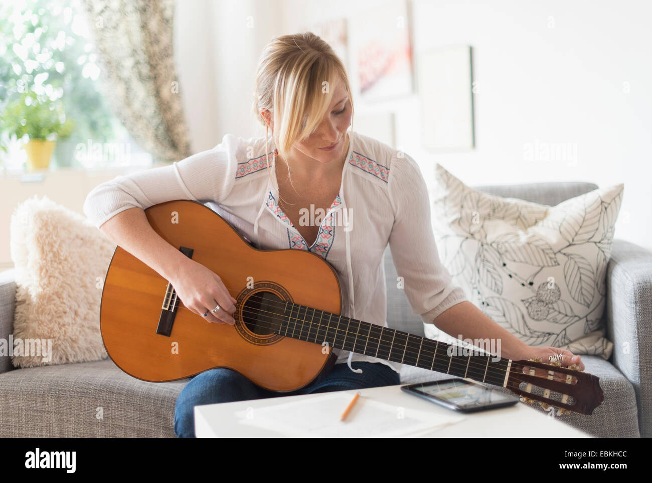 Femme assise sur un canapé et playing acoustic guitar Banque D'Images