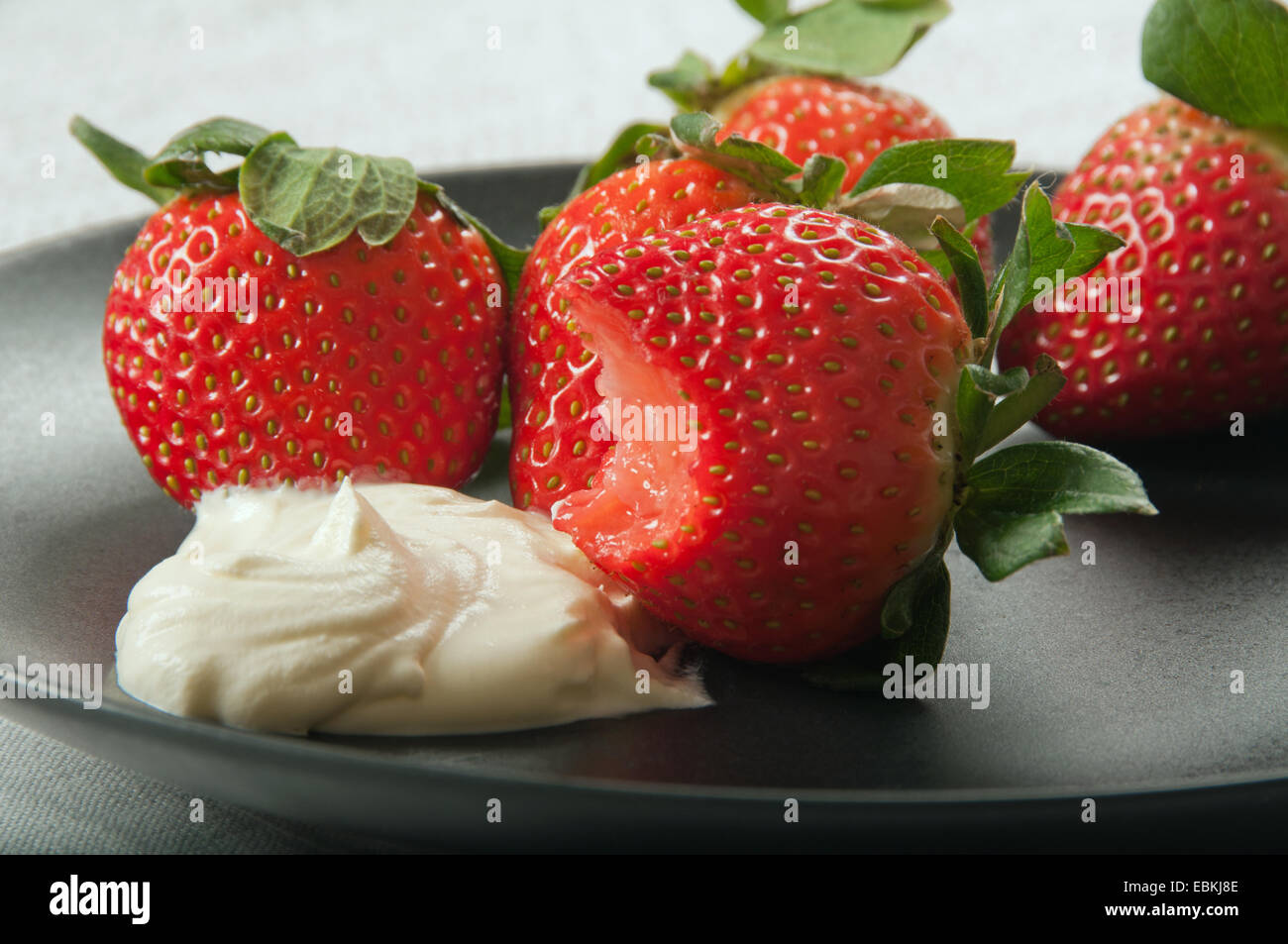 Des fraises et de la crème sur une plaque noire, une fraise avec une morsure. Banque D'Images