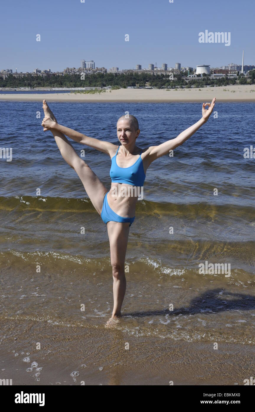 Bald woman standing in yoga position appelée-Big-Toe Hand-To prolongée Pose ou utthita hasta padangusthasana sur une plage de sable fin Banque D'Images