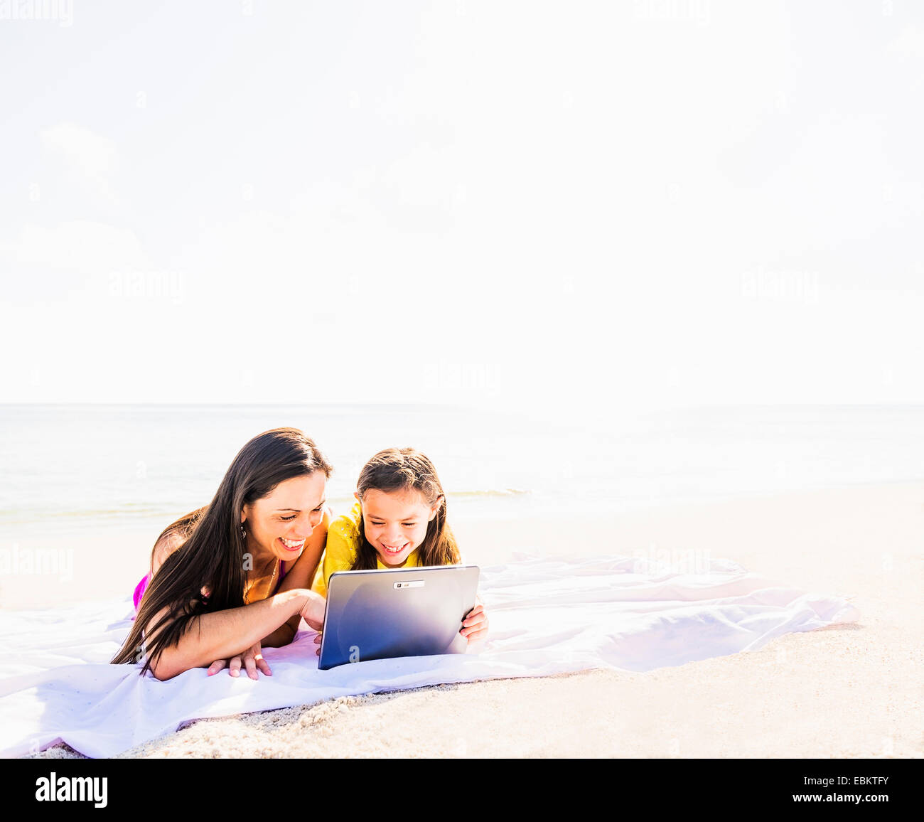 USA, Floride, Jupiter, Girl (6-7) lying on beach avec sa mère et à l'aide de tablet pc Banque D'Images