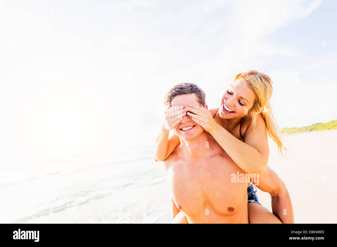 USA, Floride, Jupiter, petite amie couple on beach, fermant les yeux de petit ami avec palmiers Banque D'Images