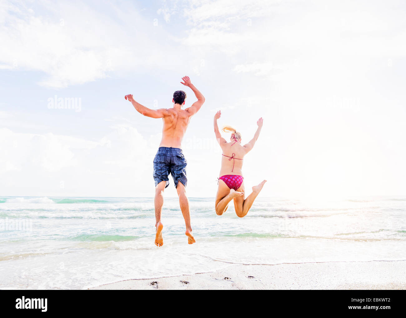 USA, Floride, Jupiter, vue arrière du jeune couple jumping on beach Banque D'Images
