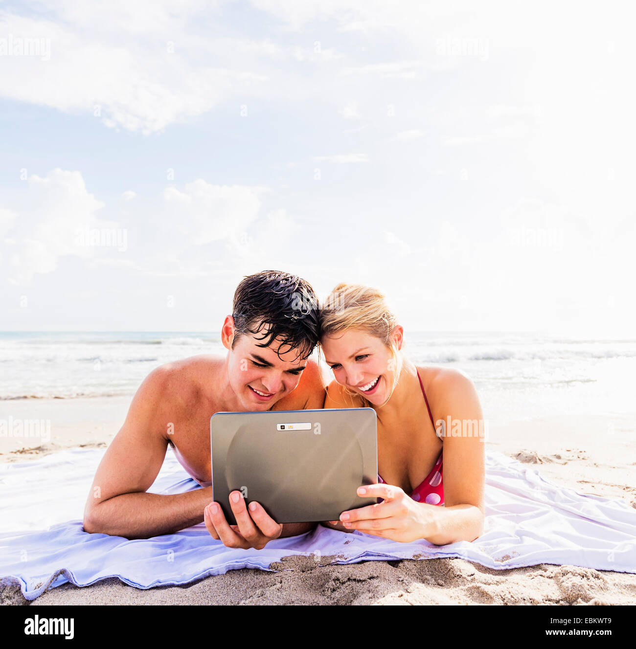 USA, Floride, Jupiter, Portrait of young couple lying on blanket sur beach côte à côte, using digital tablet Banque D'Images