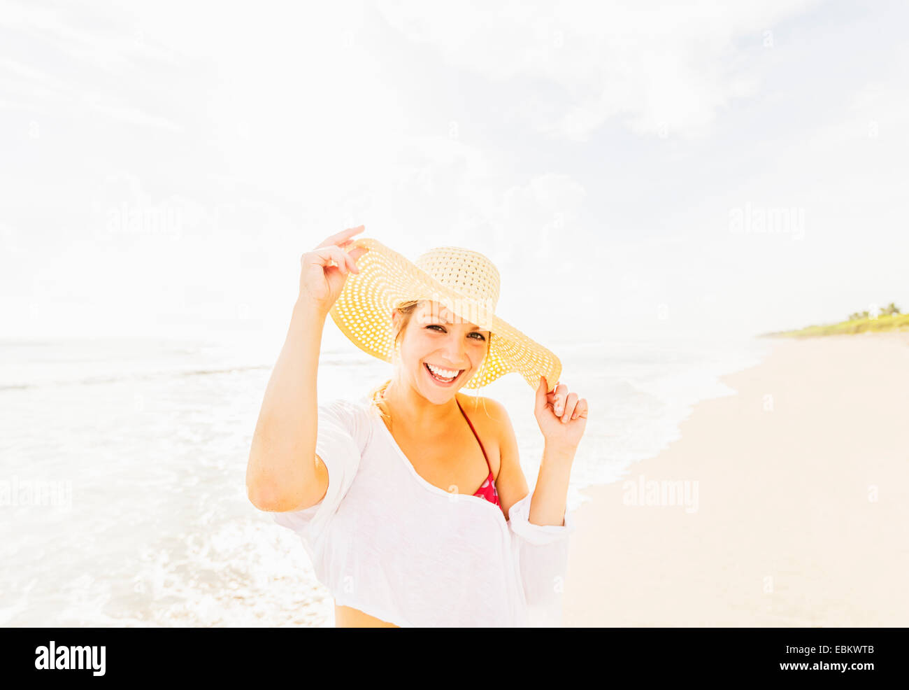 USA, Floride, Jupiter, Portrait of smiling young woman on beach wearing sun hat Banque D'Images