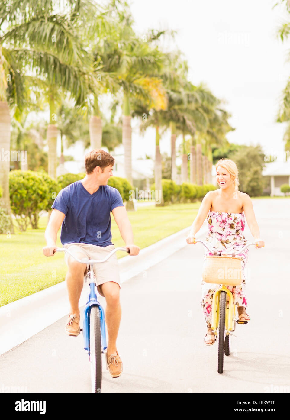 USA, Floride, Jupiter, jeune couple roulant vélos le long de rue avec palmiers Banque D'Images