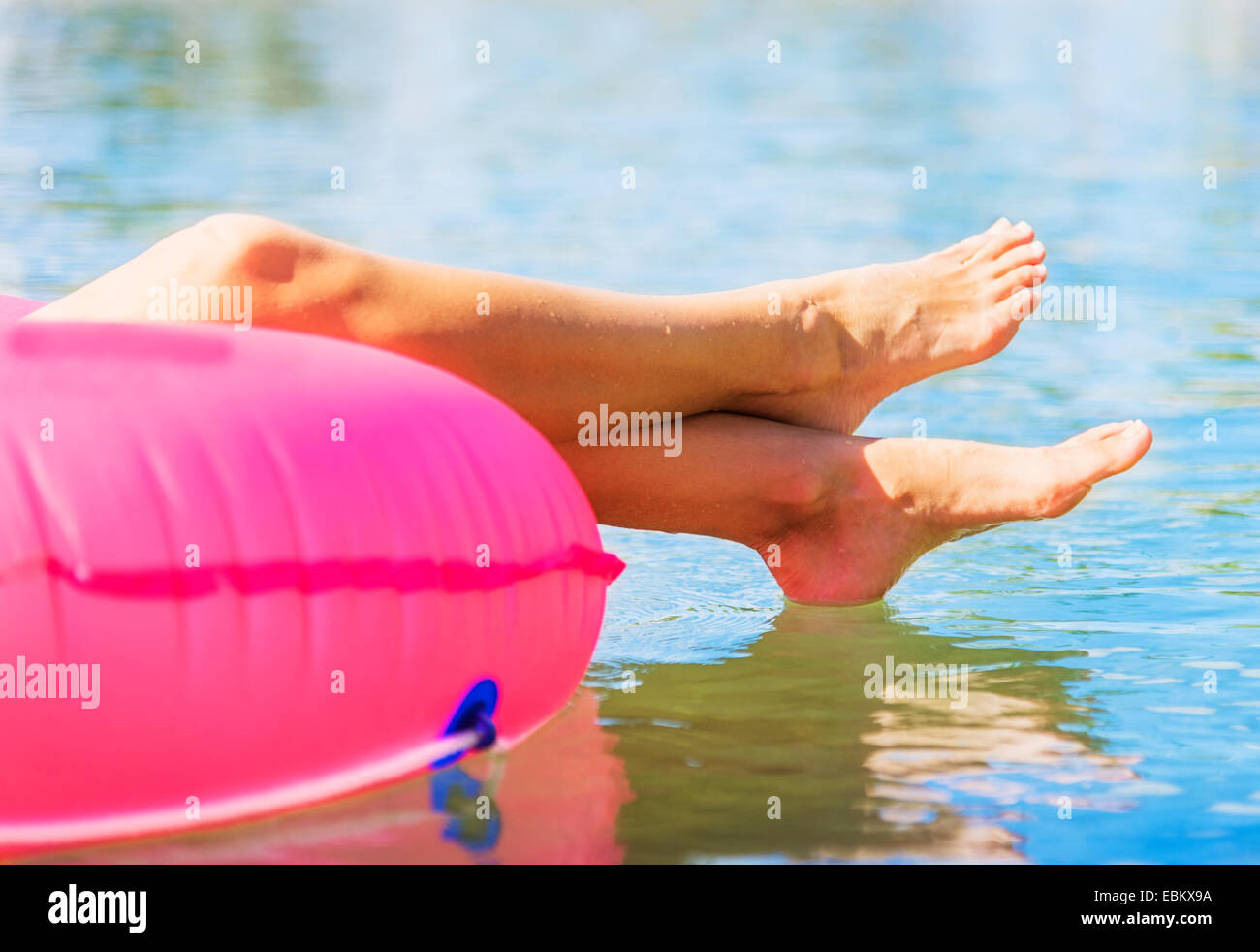 Cropped shot de jambes de jeune femme flottant sur l'anneau de bain rose Banque D'Images