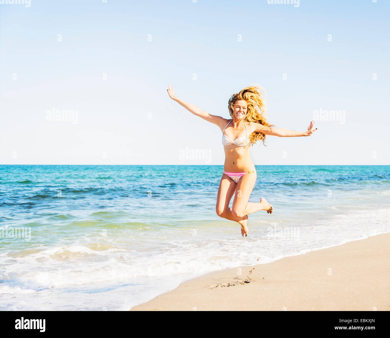 USA, Floride, Jupiter, Portrait of young woman wearing bikini jumping on beach Banque D'Images