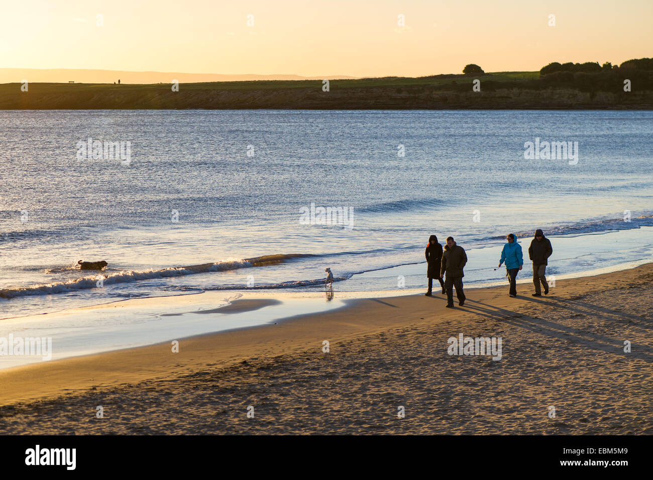 Les gens marchent le long de la plage de Barry Island, au Pays de Galles, Royaume-Uni, au coucher du soleil. Banque D'Images
