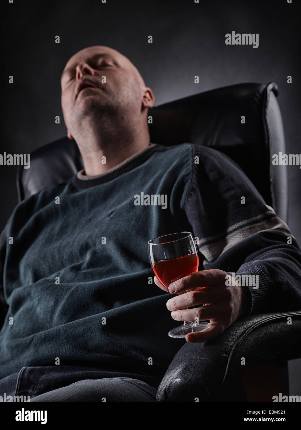 Homme d'âge moyen dort sur un fauteuil et il tenant un verre de vin, format vertical Banque D'Images