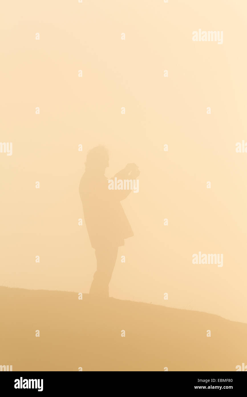 Un homme de prendre une photo sur un appareil photo compact se profile à travers le brouillard. Le soleil qui transforme le brouillard orange. Banque D'Images