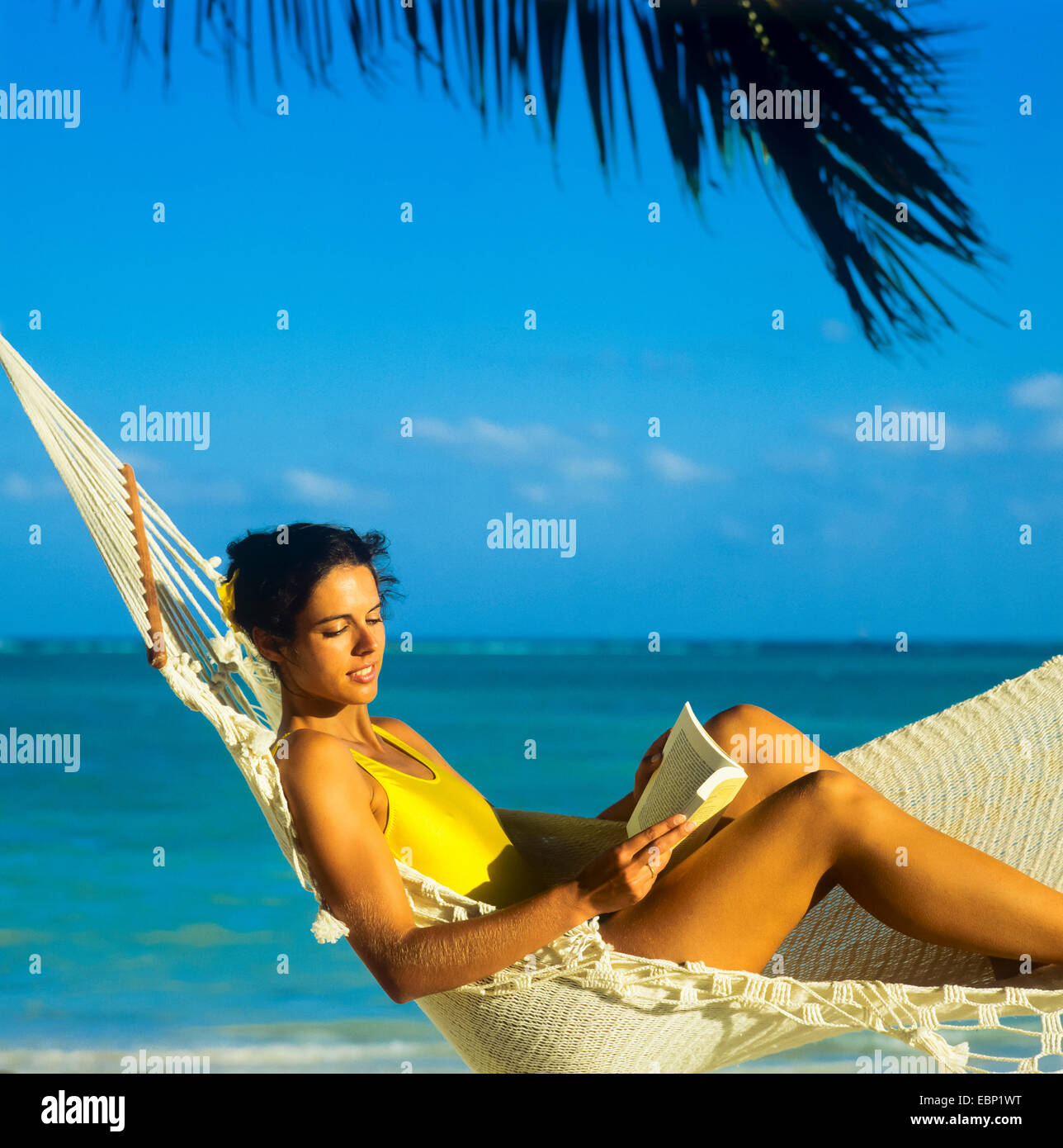 Jeune femme lisant un livre en hamac sur la plage des Caraïbes Guadeloupe Antilles Françaises Petites Antilles Banque D'Images