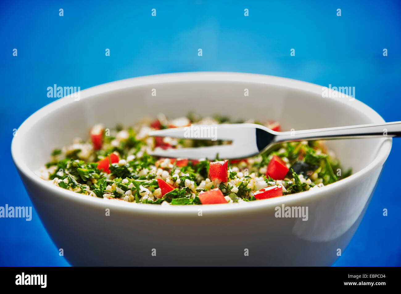 Taboulé salade dans un bol blanc sur un fond bleu foncé avec de l'argent servant d'une fourchette et cuillère Banque D'Images