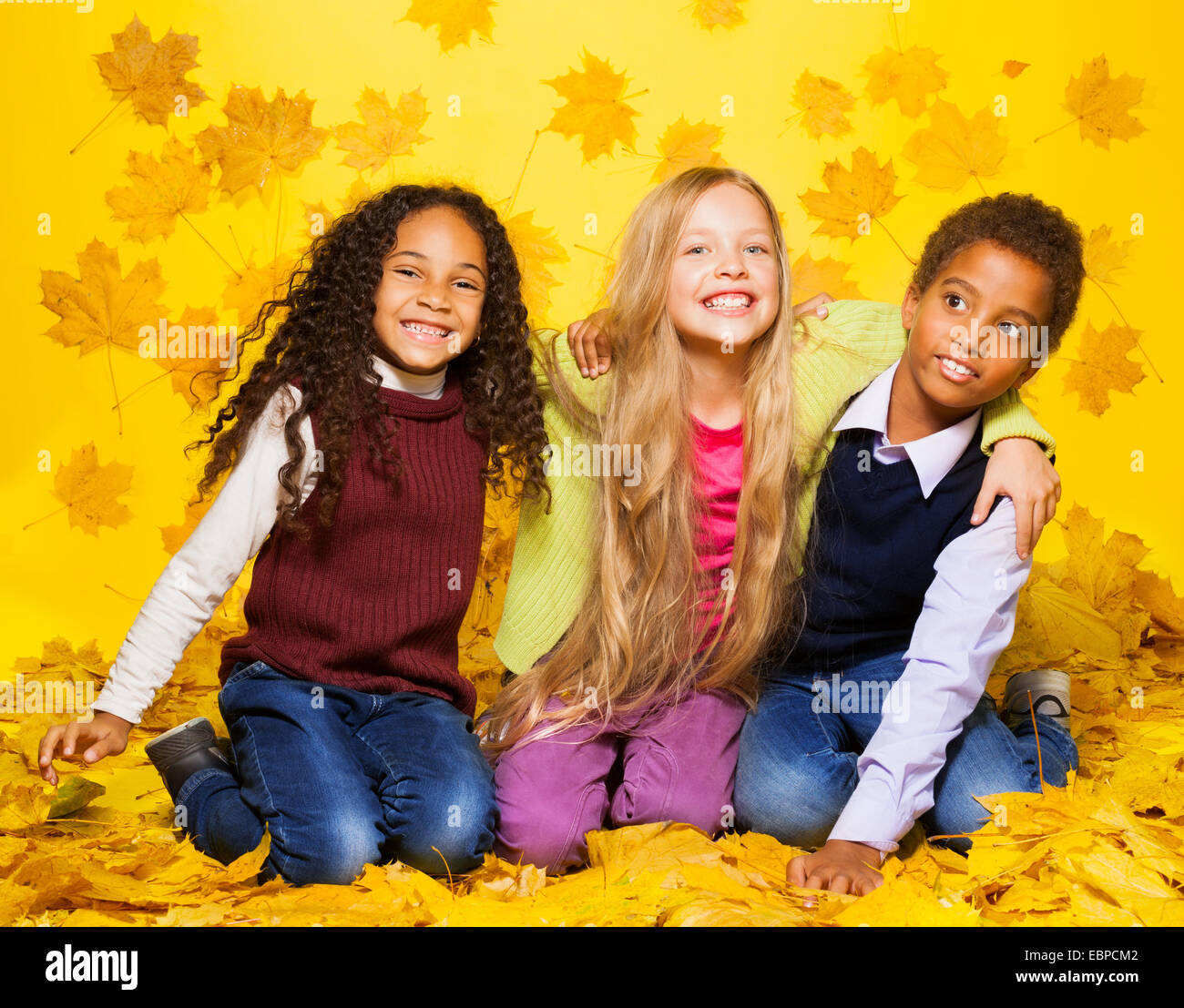 Groupe de trois enfants assis sur les feuilles d'automne Banque D'Images