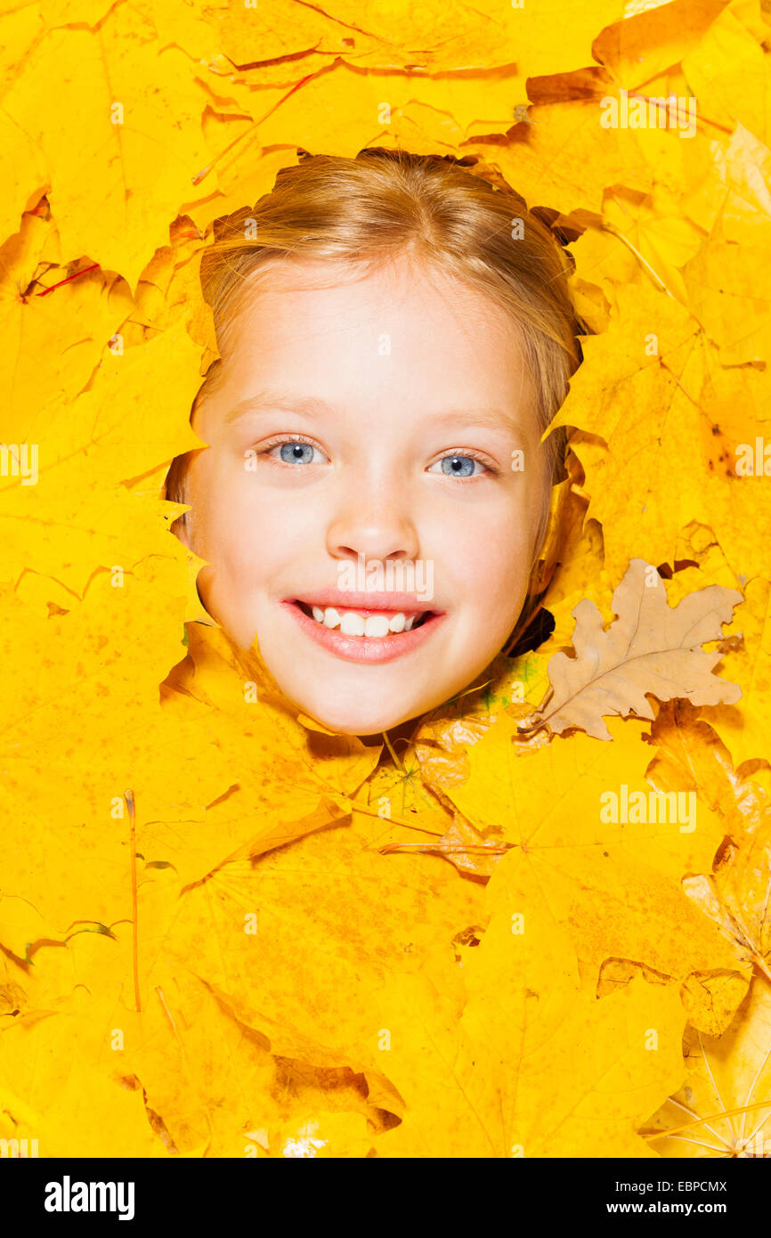 Visage d'une petite fille blonde dans les feuilles d'automne Banque D'Images