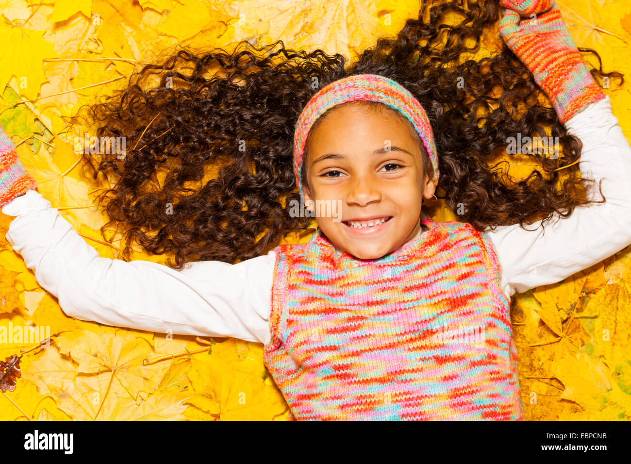Happy black fille avec des cheveux bouclés dans les feuilles d'automne Banque D'Images