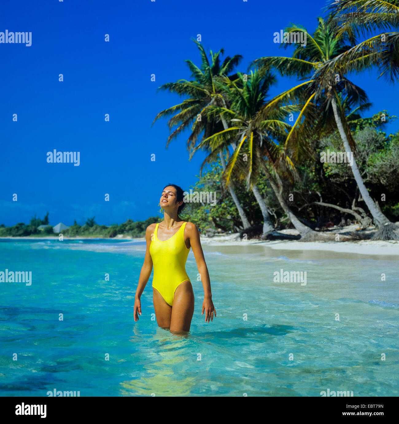 Jeune femme debout dans l'eau peu profonde de la mer des Caraïbes et plage tropicale avec palmiers Guadeloupe Banque D'Images
