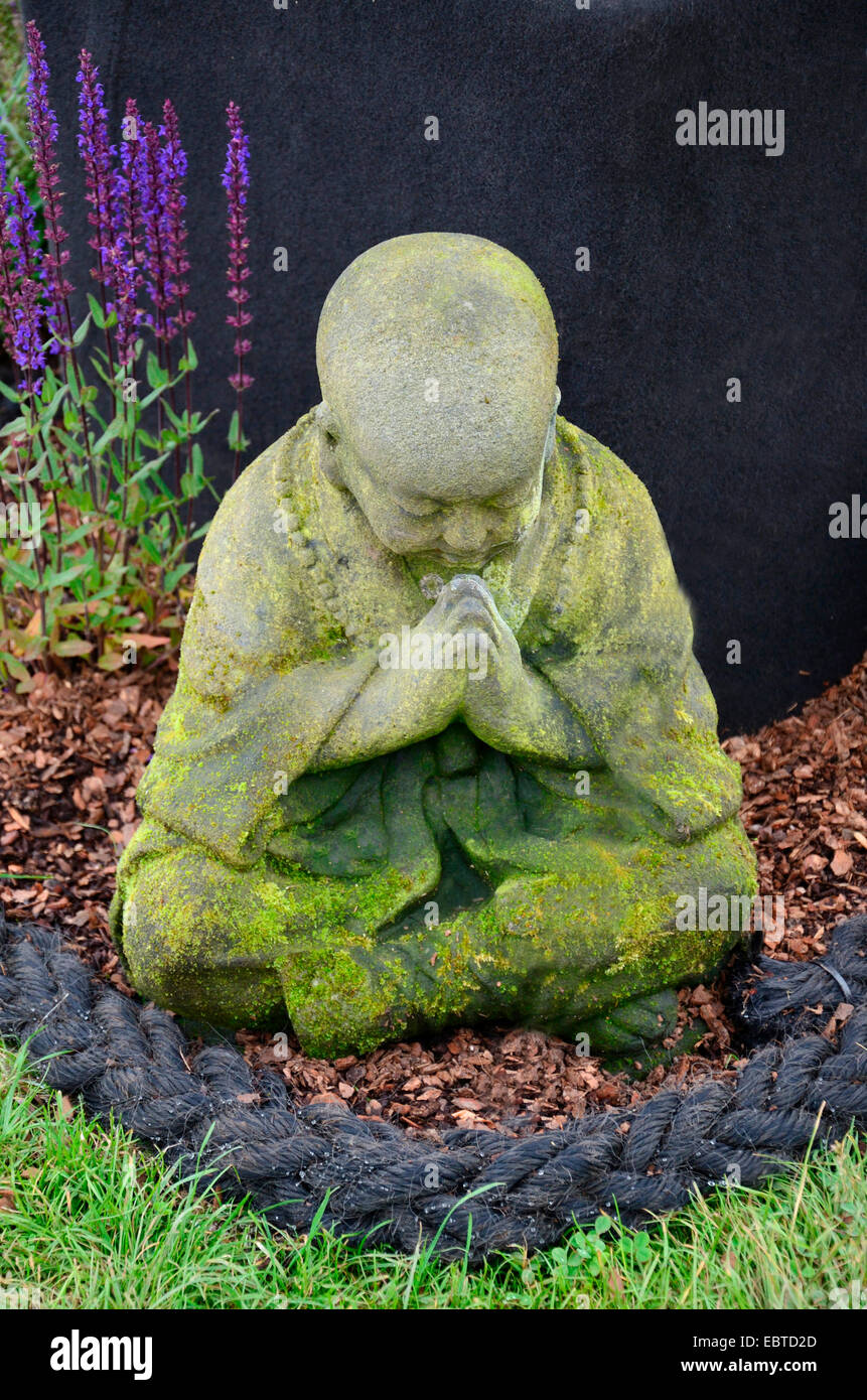 Gros plan d'une charmante enfant Bodhiolharma couverture de mousses priant dans un jardin Banque D'Images