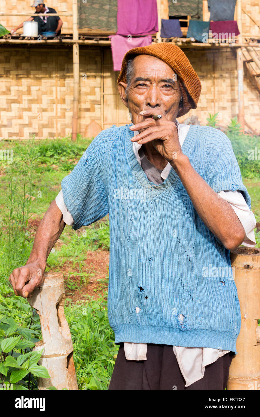 Un homme plus âgé, fumer un cigare se trouve en face de sa maison, dans un village de la tribu colline près de Kalaw en Birmanie, Myanmar, en Asie du sud-est Banque D'Images