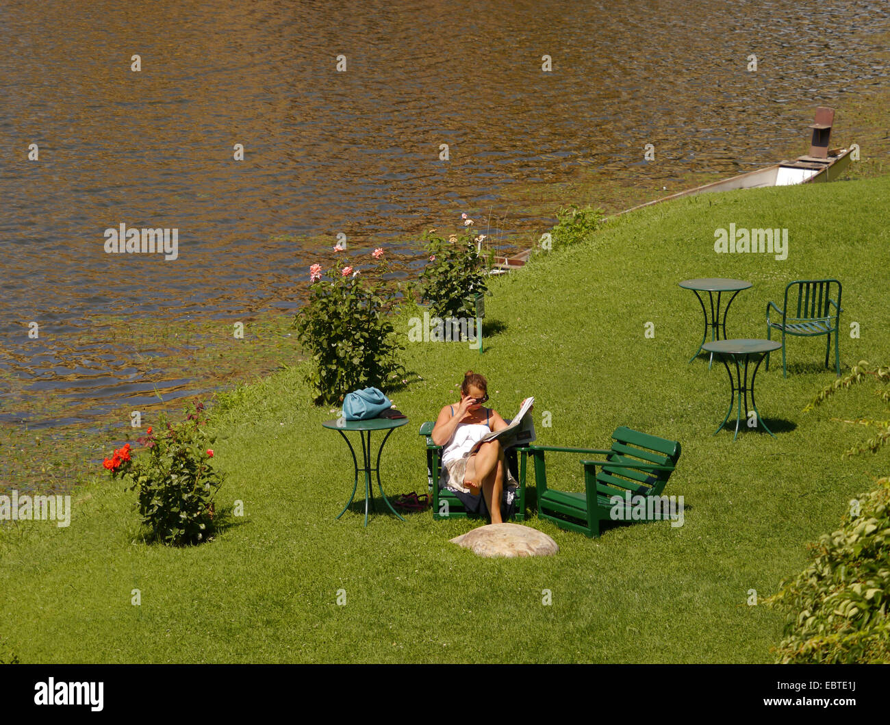 Femme lisant le papier sur une berge herbeuse en été Banque D'Images