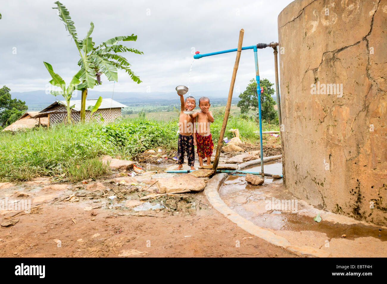 Deux jeunes garçons sont la douche d'un village communautaire, robinet et réservoir d'eau, près du lac Inle, en Birmanie, Myanmar, en Asie du sud-est Banque D'Images