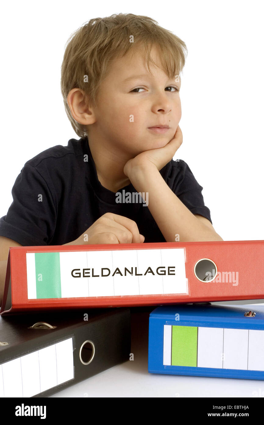 Petit garçon au sérieux s'appuyant sur un fichier avec l'inscription 'Geldanlage' ('investissement') Banque D'Images