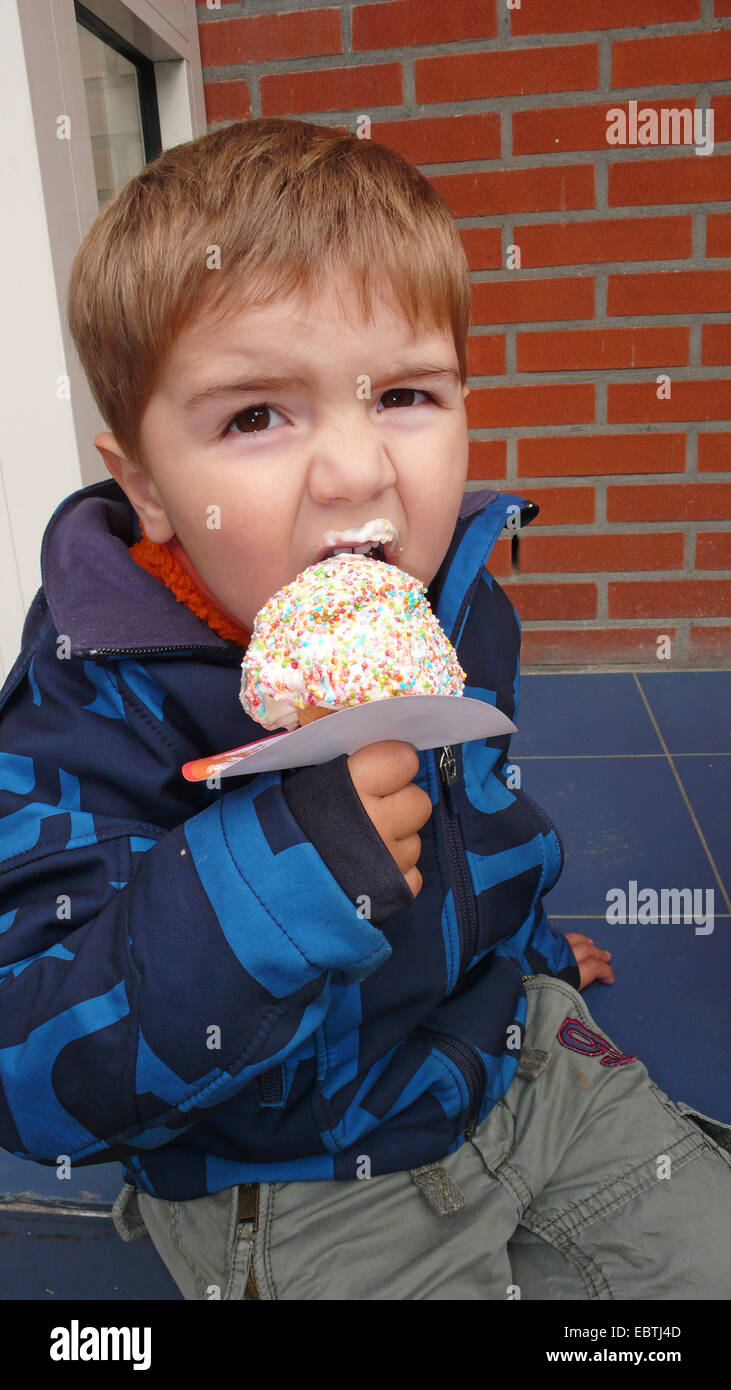 Petit garçon mangeant une glace cône avec un manchon de papier pour éviter les dribbles Banque D'Images