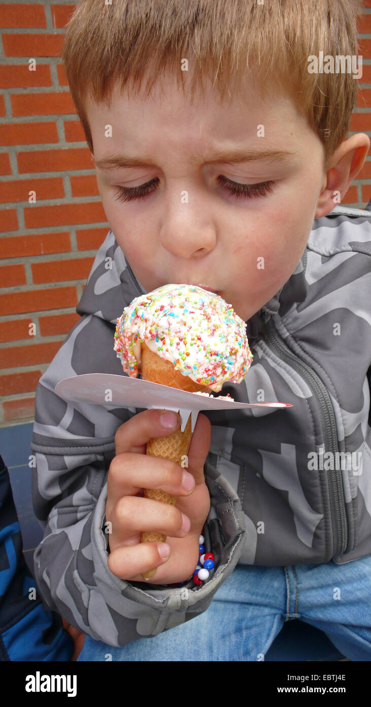 Petit garçon mangeant une glace cône avec un manchon de papier pour éviter les dribbles Banque D'Images