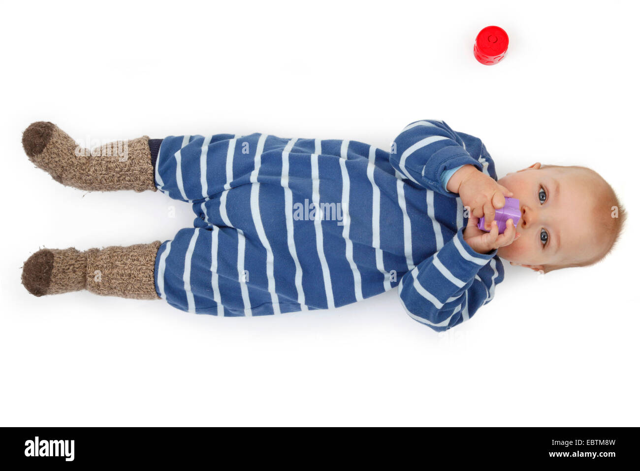 Petit enfant dans romper allongé sur le sol et en suçant à jouets bébé Banque D'Images