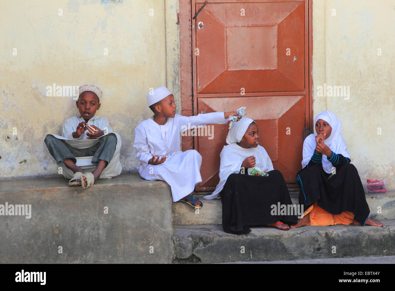 Des enfants assis en face d'une maison, la Tanzanie, Sansibar, Stone Town Banque D'Images