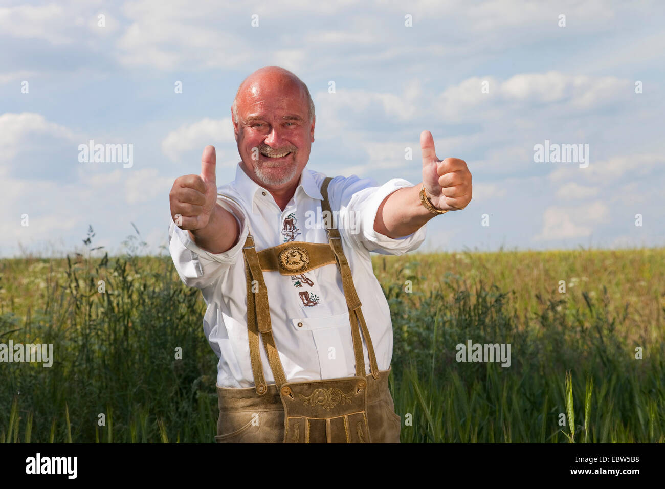 Vieux heureux homme portant costume traditionnel allemand avec Thumbs up standing in grain field, Allemagne, Rhénanie-Palatinat Banque D'Images